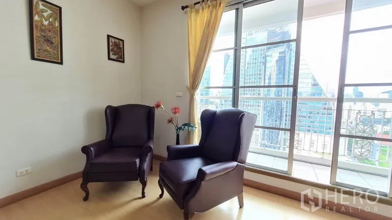 公寓 出租在Khlong Toei, Bangkok - 角落休闲区，两张翼背椅靠落地推拉门，通向阳台与天际线景色