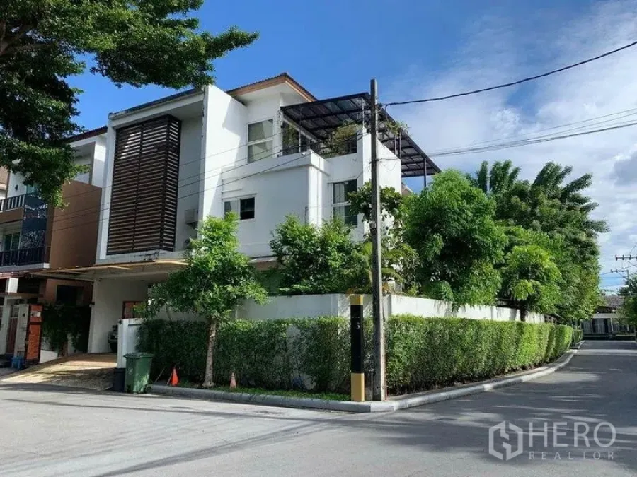 Detached House for sale in Suan Luang, Bangkok - Modern three-storey detached corner house with rooftop terrace and hedge fence on a quiet street.