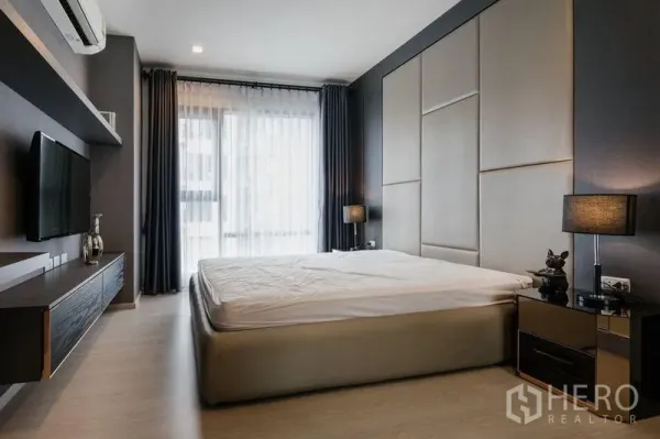 Condominium for rent in Khlong Toei, Bangkok - Master bedroom featuring an upholstered headboard, king bed, bedside lamps, and floor-to-ceiling window.