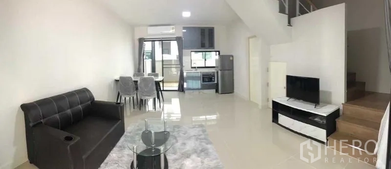 联排别墅 出租或出售在Prawet, Bangkok - 明亮的开放式客餐厅与厨房，配沙发、电视、餐桌和楼梯。