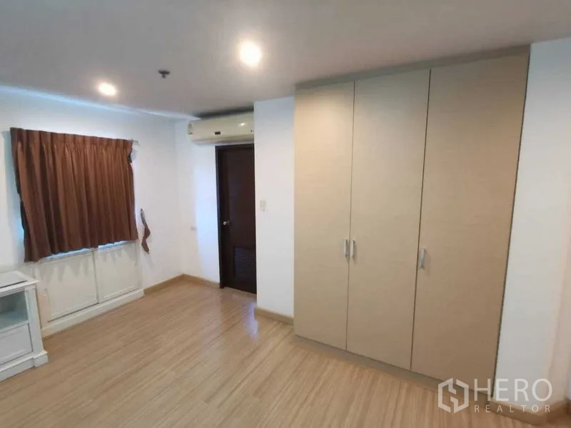 Condominium for rent in Khlong Toei, Bangkok - Spacious bedroom with bed frame, wardrobe, wood flooring and blackout curtains.