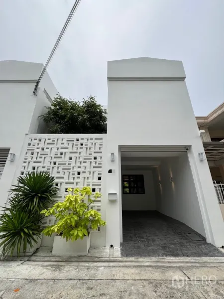 联排别墅 出售在Watthana, Bangkok - 翻新后的两层白色联排别墅立面，花格墙与有顶车位。