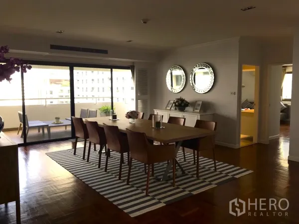 Condominium for rent in Bangkok - Dining room with long table for eight, striped rug, and glass doors to the balcony.