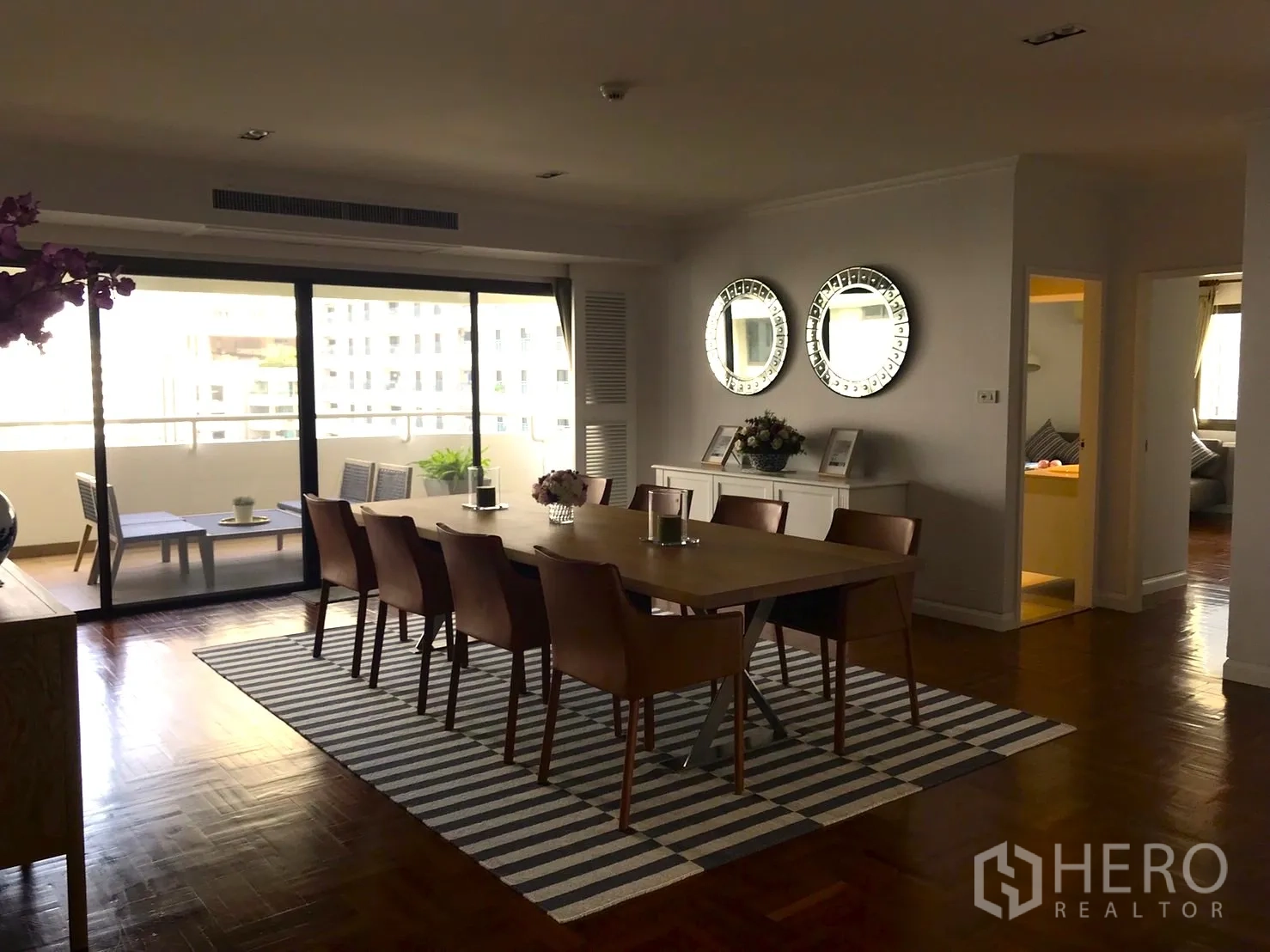Condominium for rent in Bangkok - Dining room with long table for eight, striped rug, and glass doors to the balcony.