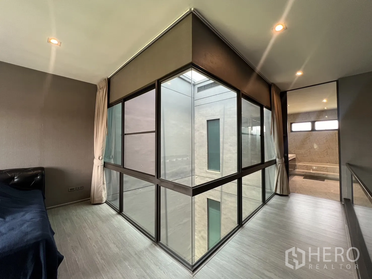 Townhouse for rent in Lat Phrao, Bangkok - Upper hallway with floor-to-ceiling corner glazing looking into the atrium and bathroom beyond.