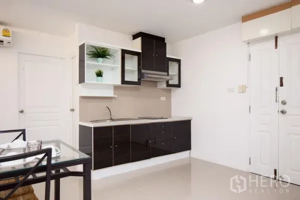 Condominium for rent in Khlong Toei, Bangkok - Compact kitchenette with black cabinets, cooktop, range hood and open shelves by the entry.