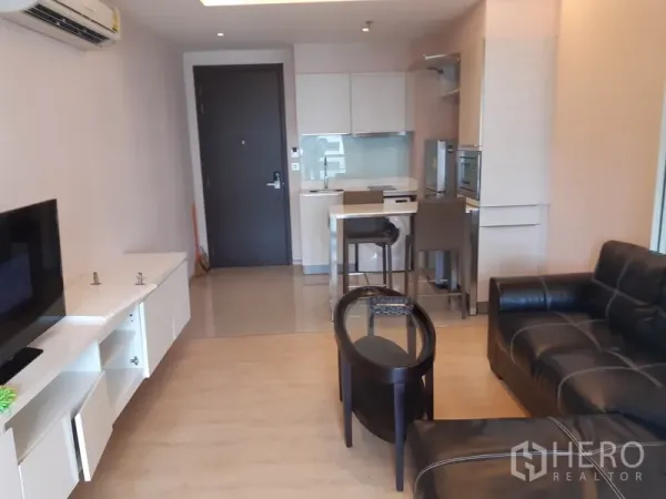 Condominium for rent in Watthana, Bangkok - Open-plan lounge facing a compact kitchen with breakfast counter, modern cabinetry, and the entry door.