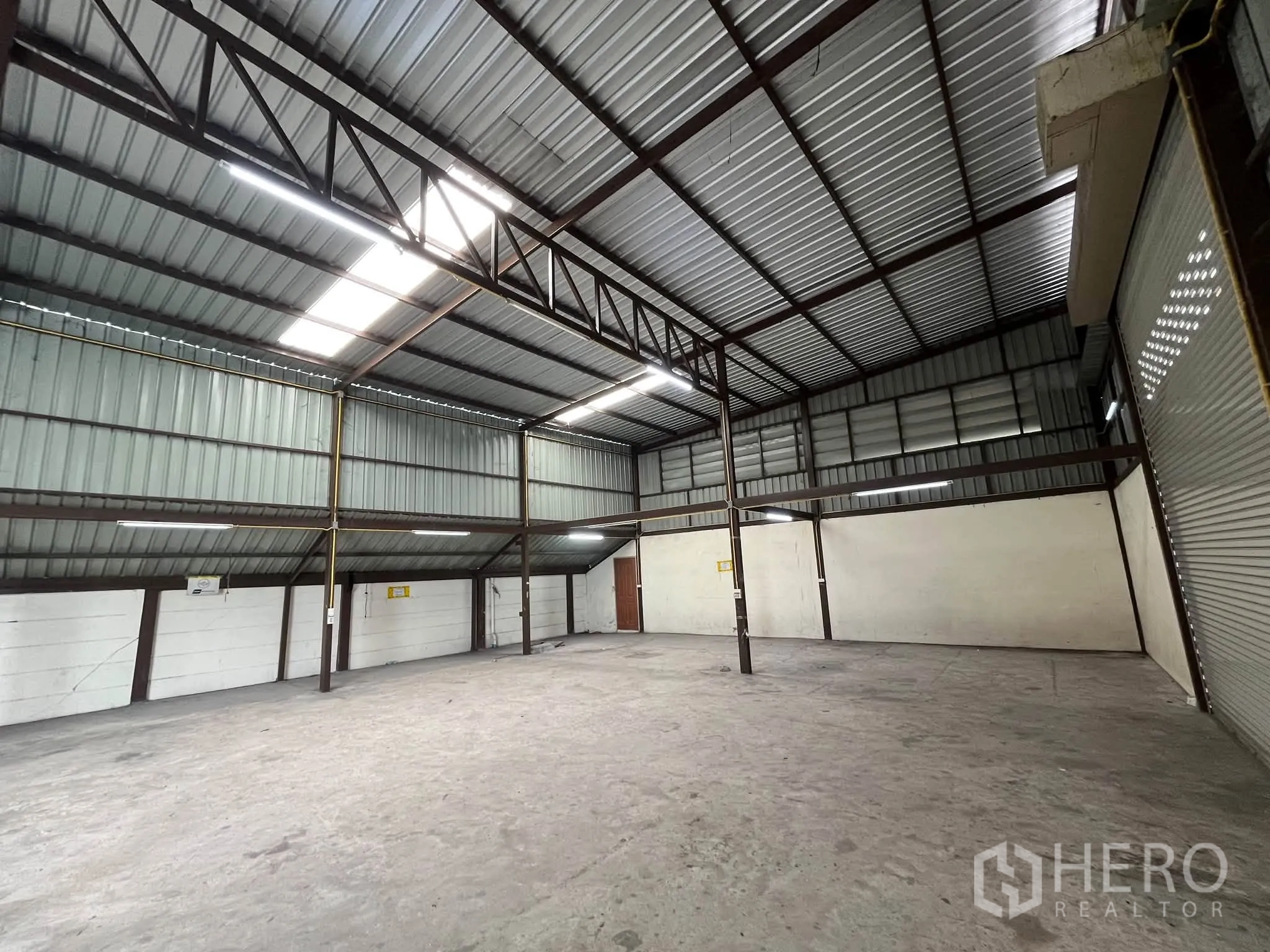 โกดัง for rent in Prawet, Bangkok - พื้นที่เก็บสินค้าที่โล่ง มีประตูม้วน ทางเข้าโหลดของ และไฟส่องสว่างบนเพดาน.