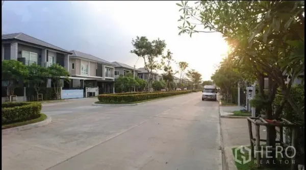 Detached House for sale in Bang Yai, Nonthaburi - Tree-lined residential street of a gated estate with two-storey houses at sunset