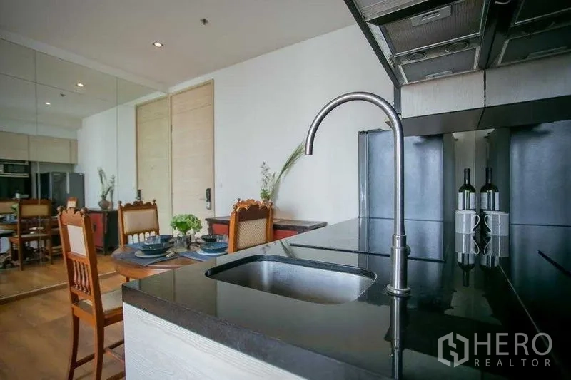 Condominium for sale in Khlong Toei, Bangkok - Close-up of black stone countertop and curved faucet at the condo kitchen sink.