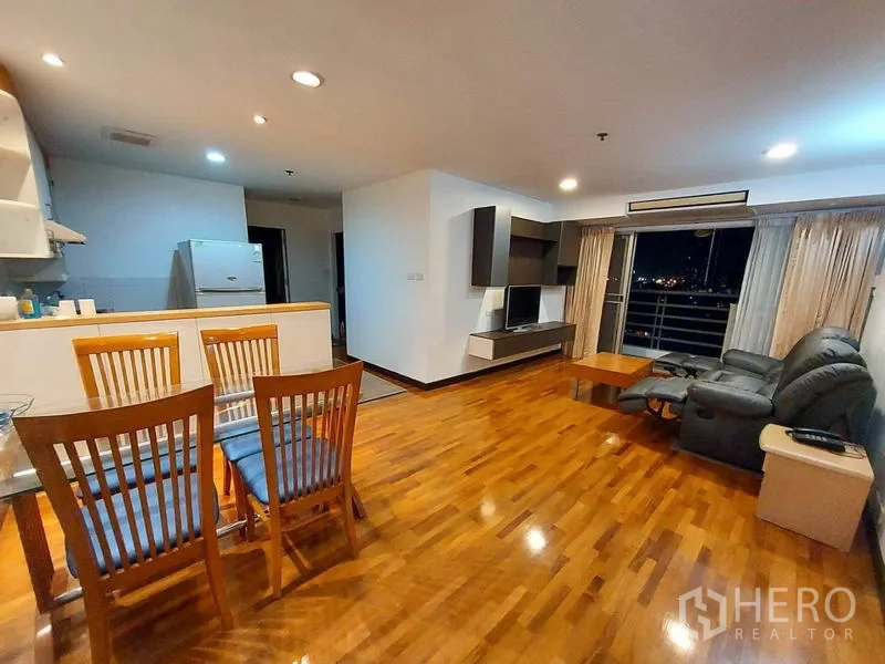 Condominium for rent or sale in Khlong Toei, Bangkok - Open-plan living and dining room with hardwood floors, TV wall and balcony city view at night.