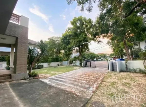 Detached House for sale in Saphan Sung, Bangkok - Wide driveway and gated entrance with lawn and mature trees in a quiet estate.