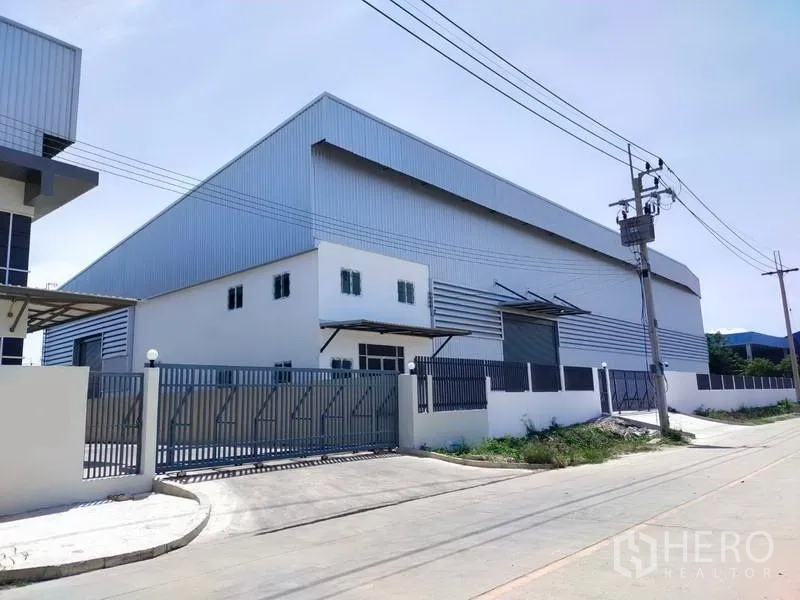 Factory for rent in Samut Prakan - Modern steel-clad factory exterior with gated entrance on a wide road in Bang Pu.