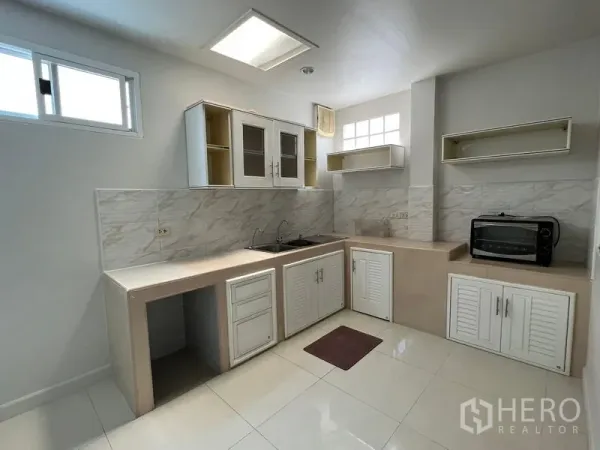 Detached House for rent in Bang Kapi, Bangkok - Bright L-shaped kitchen with white cabinets, tiled backsplash and windows.