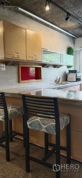 Condominium for sale in Watthana, Bangkok - Modern kitchen with breakfast bar, granite countertop, two bar stools and upper cabinets in a Watthana condo.