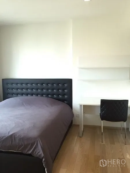 Condominium for rent in Khlong Toei, Bangkok - Cozy bedroom with upholstered headboard, desk and chair on light wood flooring.