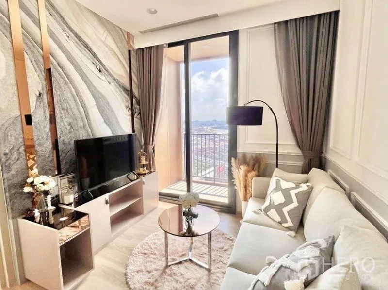 Condominium for rent in Khlong Toei, Bangkok - Bright living room with marble feature wall, TV console and sliding glass doors opening to a balcony with skyline views.