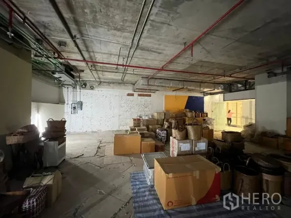Retail Space for rent - Unfinished shop space with open layout, exposed services and boxes near a glass-fronted corridor.