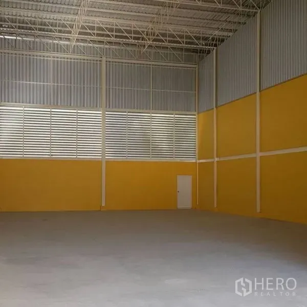 Warehouse for rent in Mueang Samut Prakan, Samut Prakan - High-clearance warehouse interior with steel trusses, louvered ventilation panels, yellow walls and a smooth concrete floor.