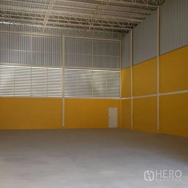 Warehouse for rent in Mueang Samut Prakan, Samut Prakan - High-clearance warehouse interior with steel trusses, louvered ventilation panels, yellow walls and a smooth concrete floor.