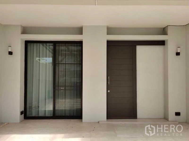 Townhouse for rent in Suan Luang, Bangkok - Close-up of the main entrance with sliding glass door and a solid wood front door