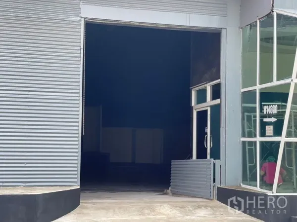 Warehouse for rent in Sam Phran, Nakhon Pathom - Loading bay view showing a large roller shutter and adjacent glass side door.