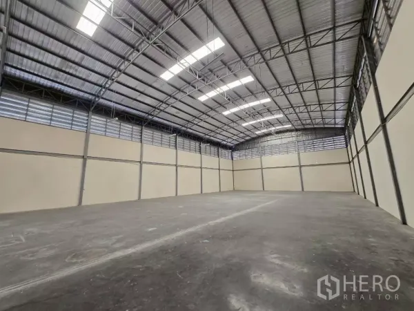 Factory for rent or sale in Mueang Samut Sakhon, Samut Sakhon - Spacious clear-span warehouse interior with high steel truss roof, ventilation louvers and concrete floor.