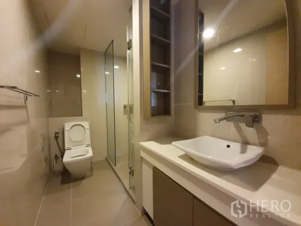 公寓 出租在Watthana, Bangkok - 现代浴室，台上盆、收纳柜、坐便器与玻璃淋浴间。