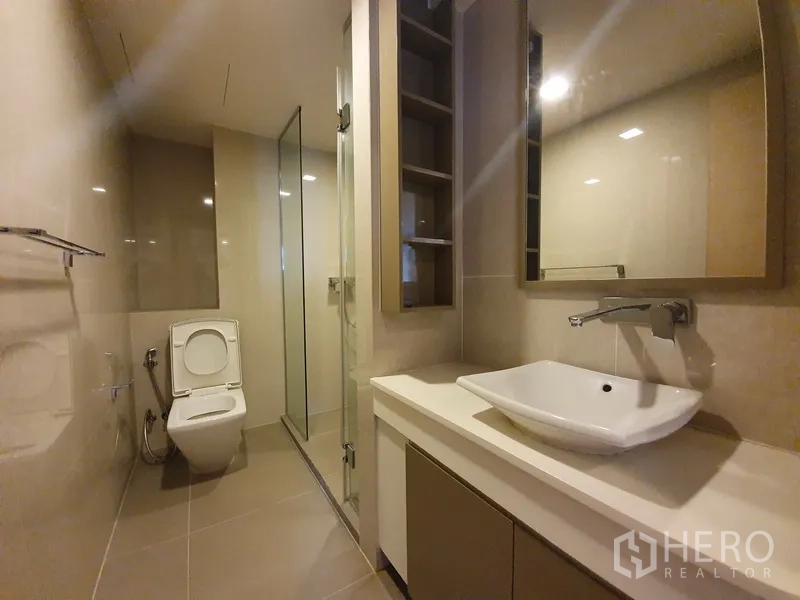 公寓 出租在Watthana, Bangkok - 现代浴室，台上盆、收纳柜、坐便器与玻璃淋浴间。