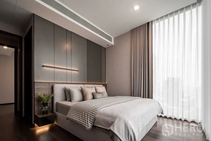 Condominium for rent in Watthana, Bangkok - Modern master bedroom with upholstered bed, grey panel wall and large window with sheer drapes.