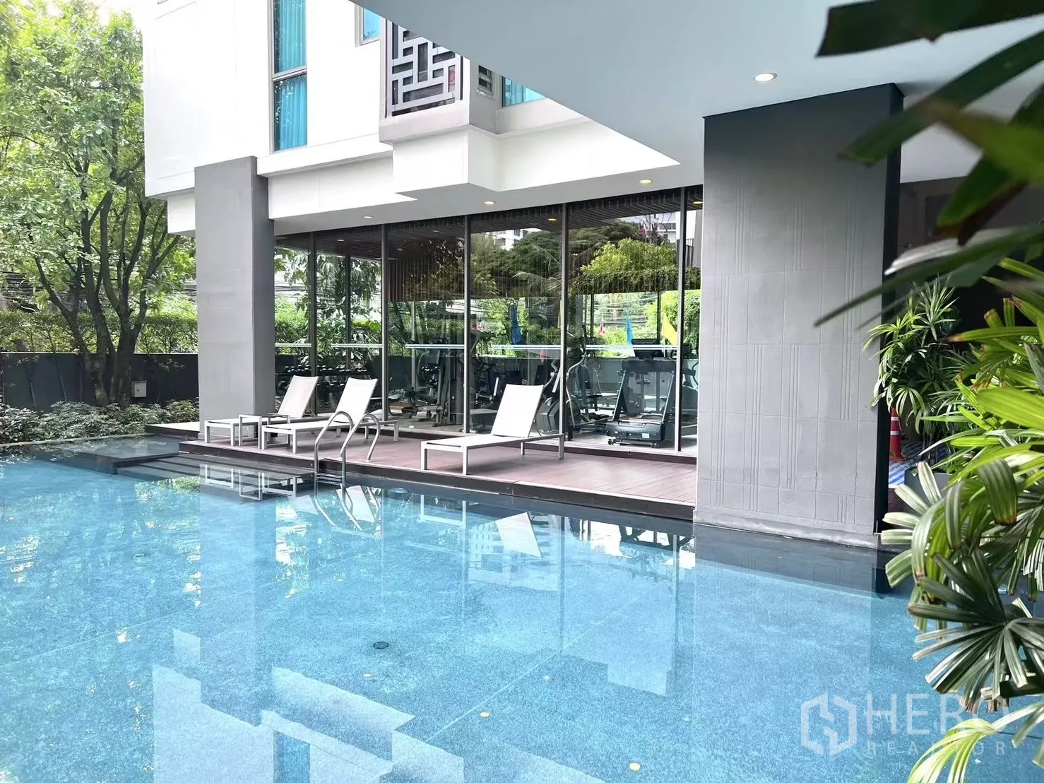 公寓 出售在Watthana, Bangkok - 室外泳池配躺椅，旁连健身房，绿意环绕。