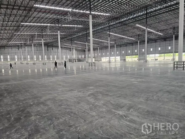 工厂 出租在Chon Buri - 超大仓库内部，抛光混凝土地面，高位桁架屋顶与成排钢柱。