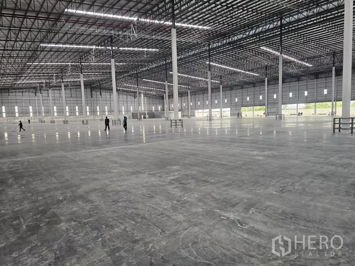 工厂 出租在Chon Buri - 超大仓库内部，抛光混凝土地面，高位桁架屋顶与成排钢柱。