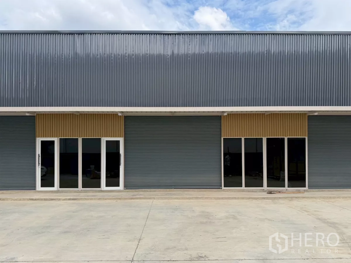 Warehouse for rent in Suan Luang, Bangkok - Facade of a new steel-clad warehouse with roller shutters, glass doors and a wide concrete forecourt in Suan Luang, Bangkok.