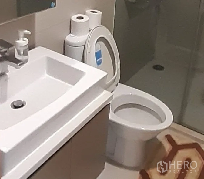 Condominium for rent in Khlong Toei, Bangkok - Contemporary bathroom with vanity sink, toilet and glass-enclosed shower.