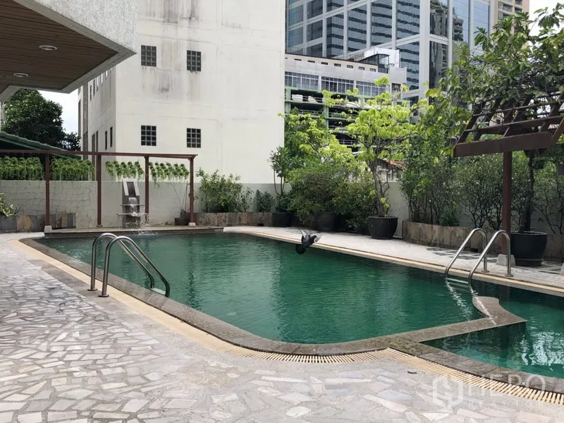 Condominium for rent in Khlong Toei, Bangkok - Condominium outdoor swimming pool surrounded by greenery and seating.