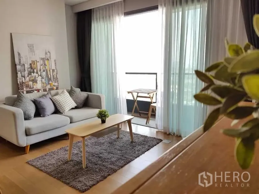 Condominium for rent in Khlong Toei, Bangkok - Living room opening to a balcony with city view, gray rug and wall art.