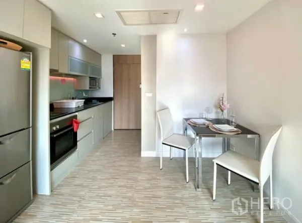 Condominium for rent in Khlong Toei, Bangkok - Open-plan kitchen with oven, microwave, ample cabinets, and an adjacent dining area.