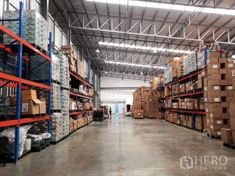 Warehouse for rent or sale in Nonthaburi - Wide warehouse aisle lined with tall steel racks and boxed inventory.