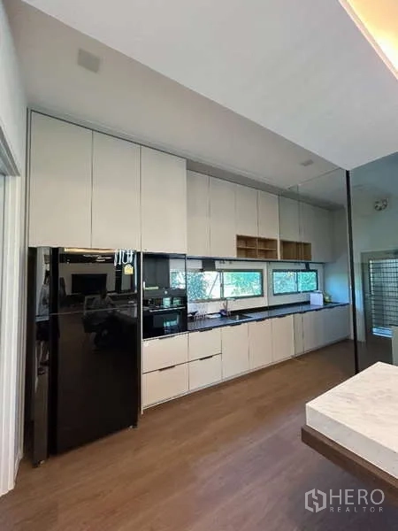 Detached House for rent in Saphan Sung, Bangkok - Full-length white kitchen cabinetry with black fridge and window backsplash.
