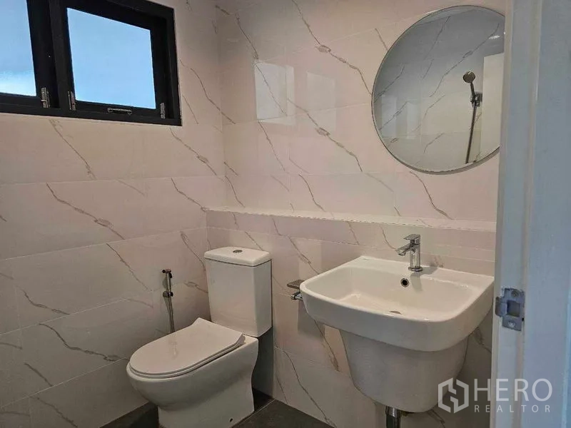 Detached House for sale in Thanyaburi, Pathum Thani - Compact bathroom with tiled walls, toilet, basin, and round mirror.
