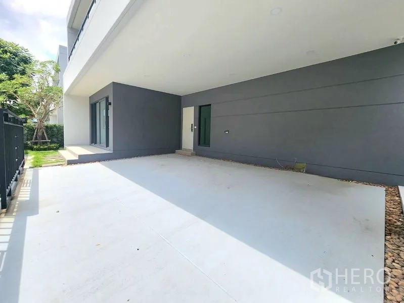 Detached House for rent in Bang Phli, Samut Prakan - Covered carport with concrete floor beside a small lawn and sliding doors.