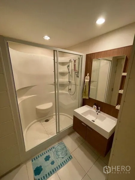Condominium for sale - Compact bathroom with glass-enclosed shower, vanity and storage shelves.