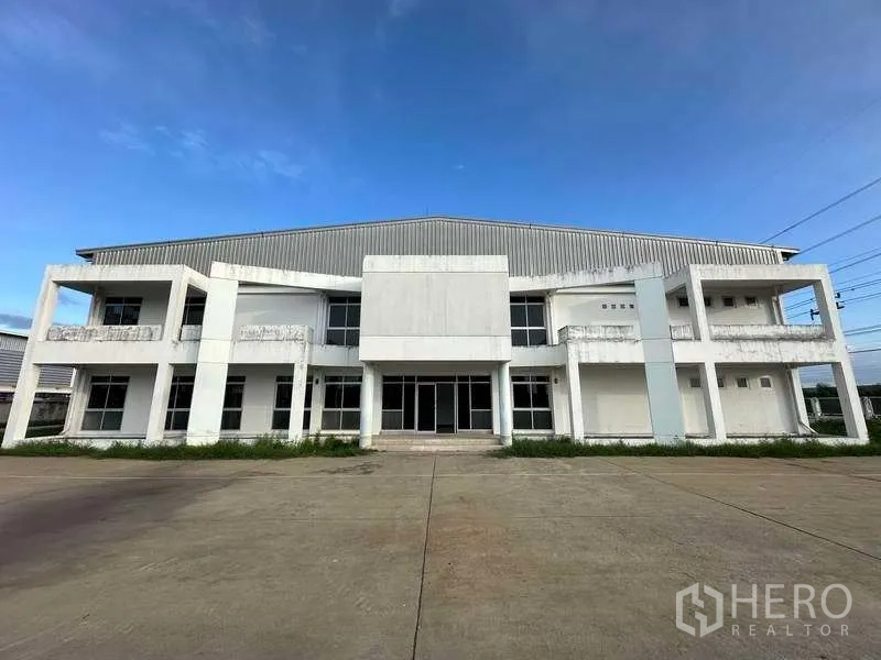 Factory for rent in Khlong Luang, Pathum Thani - Front facade of a large factory building with columned entrance and expansive parking apron.