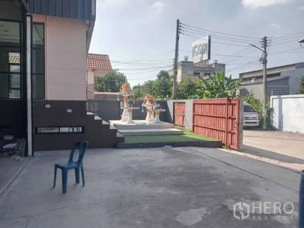 Warehouse for rent in Lam Luk Ka, Pathum Thani - Concrete forecourt with red sliding gate and a small raised platform beside the office wing.