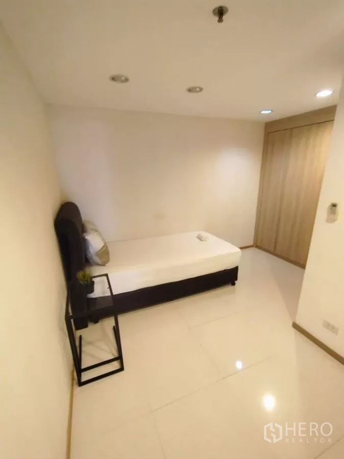 Condominium for rent in Khlong Toei, Bangkok - Second bedroom with single bed, side table, and built-in wardrobe.