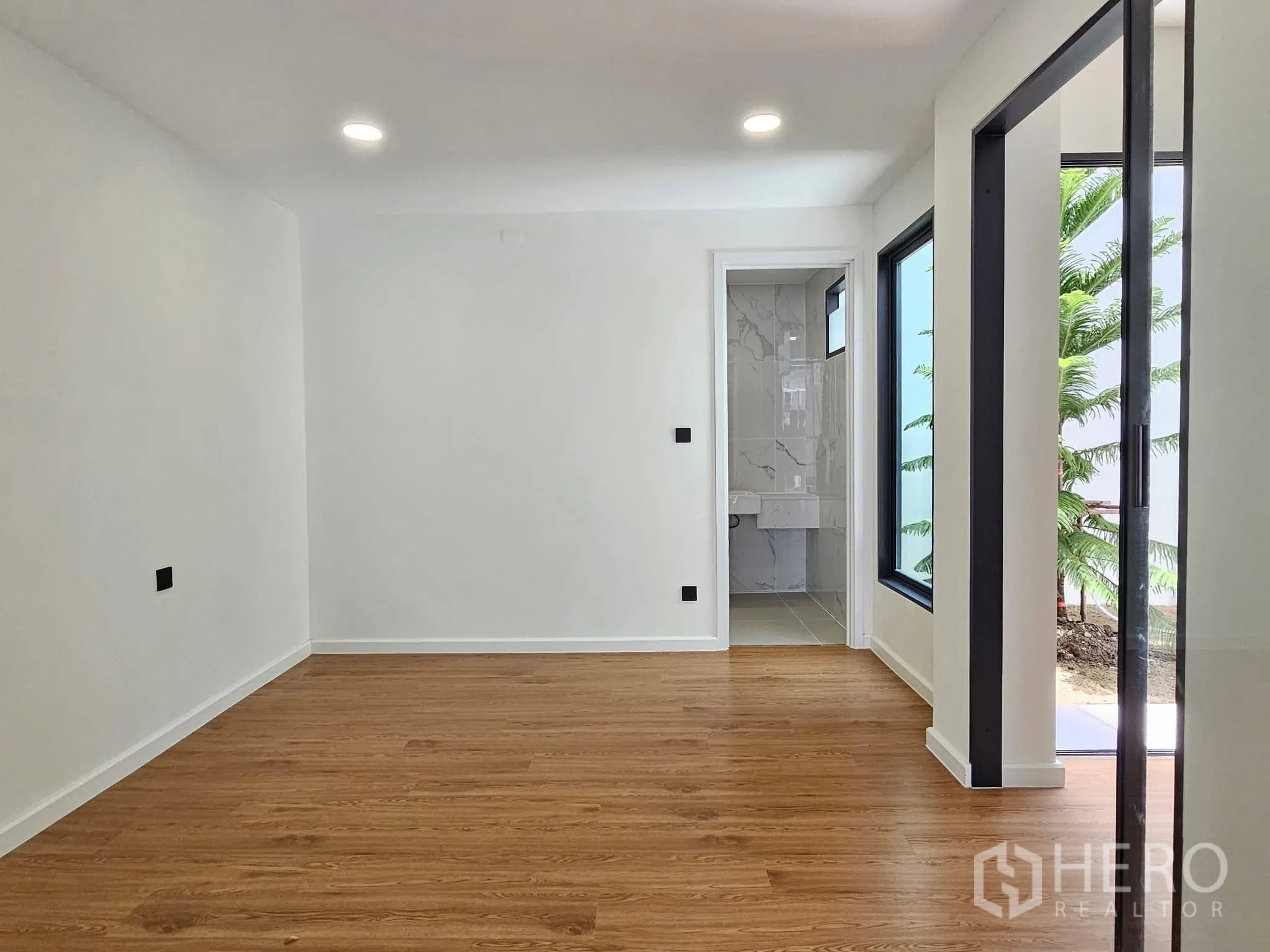 独栋房屋 for sale in Lat Phrao, Bangkok - 一层房间，木纹地板，带卫浴入口并可望见花园。