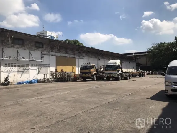 货栈 出租在Khlong Toei, Bangkok - 宽阔的混凝土场地，卡车停靠在带装卸雨棚的单层仓库前
