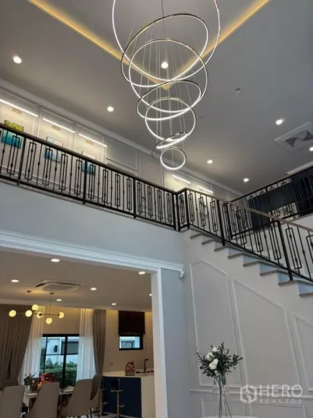 บ้าน ให้เช่าในBang Phli, Samut Prakan - มุมใกล้ของโคมไฟระย้าวงแหวนและทางเดินชั้นลอยเหนือห้องนั่งเล่น.