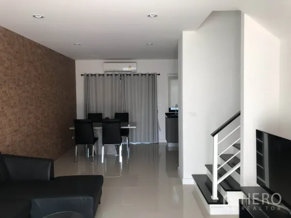 联排别墅 出租在Bang Kapi, Bangkok - 开放式客餐厅，砖纹特色墙、亮面地砖与通往二楼的楼梯，可见紧凑厨房。